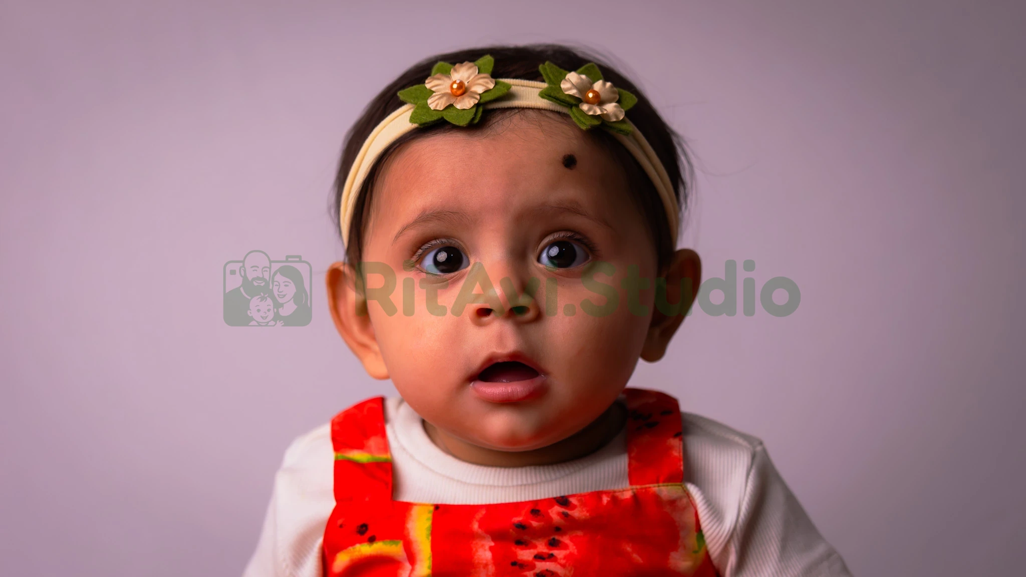 Wide-eyed baby in orange dungarees and a floral headband in Gurugram